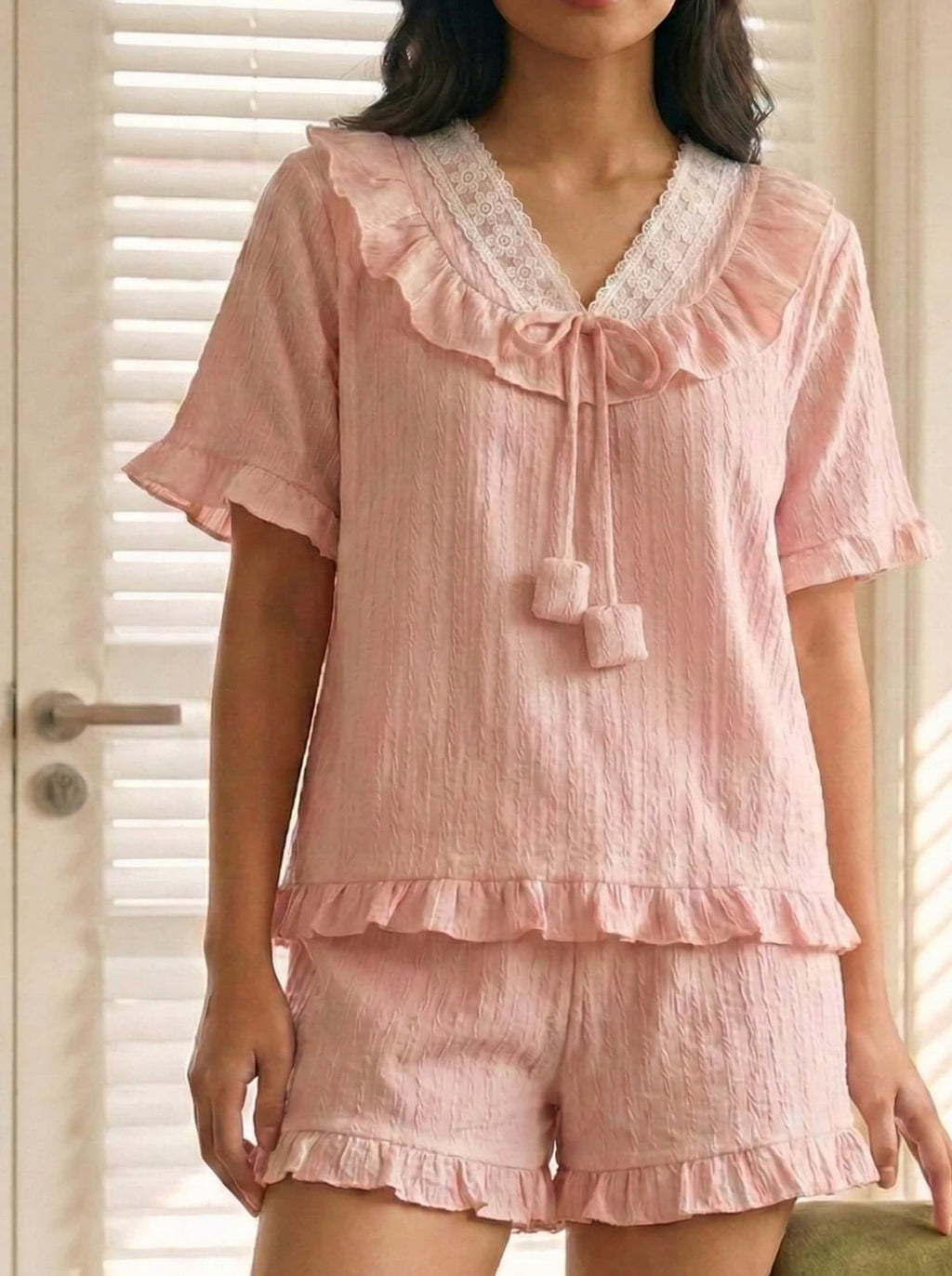 Pink pajama set with ruffles and lace details worn by a person.